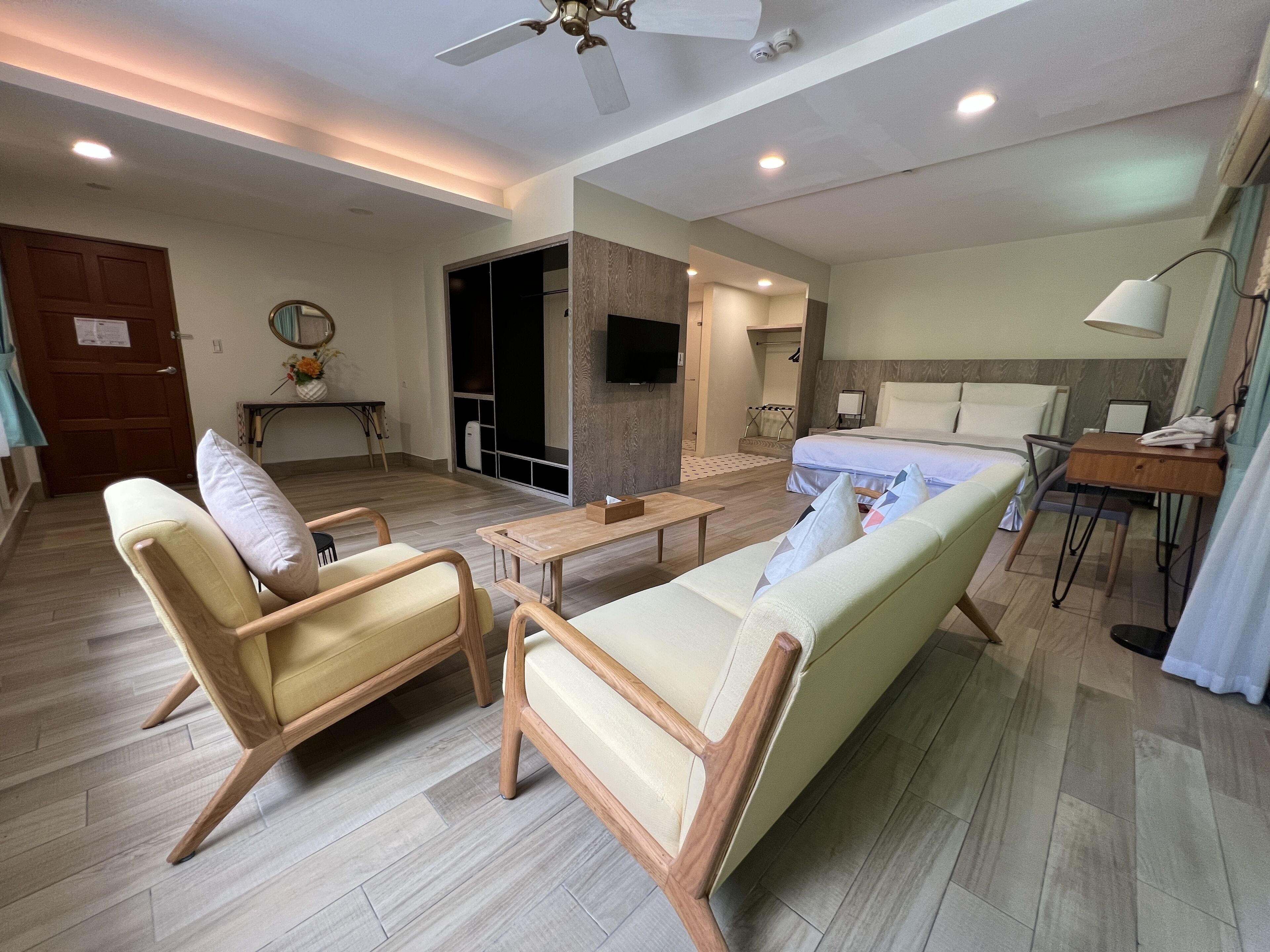 Una habitación de hotel moderna con sofá, sillones, escritorio, cama y televisor.