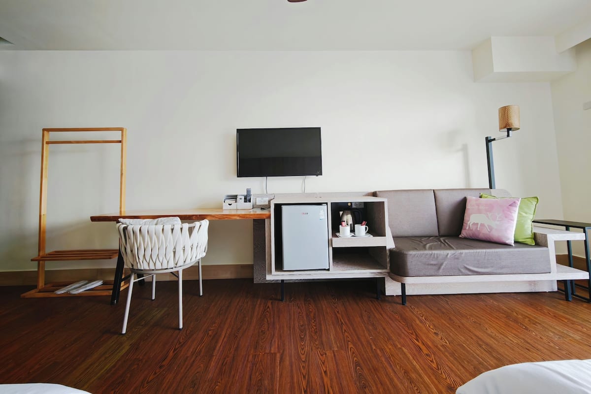 Een moderne hotelkamer met een houten vloer, een bank, een televisie, een bureau met stoel en een lamp.