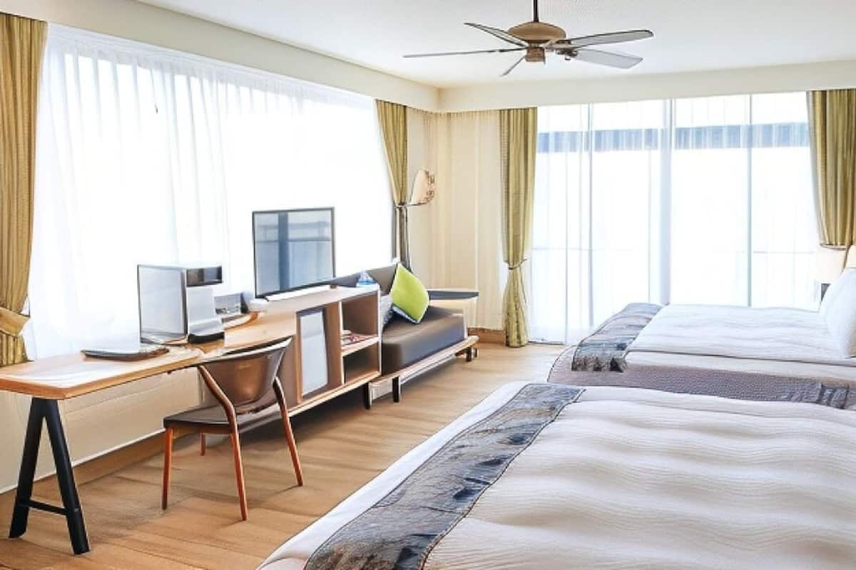 Een hotelkamer met twee bedden, een bureau met een computer, een televisie en een plafondventilator.