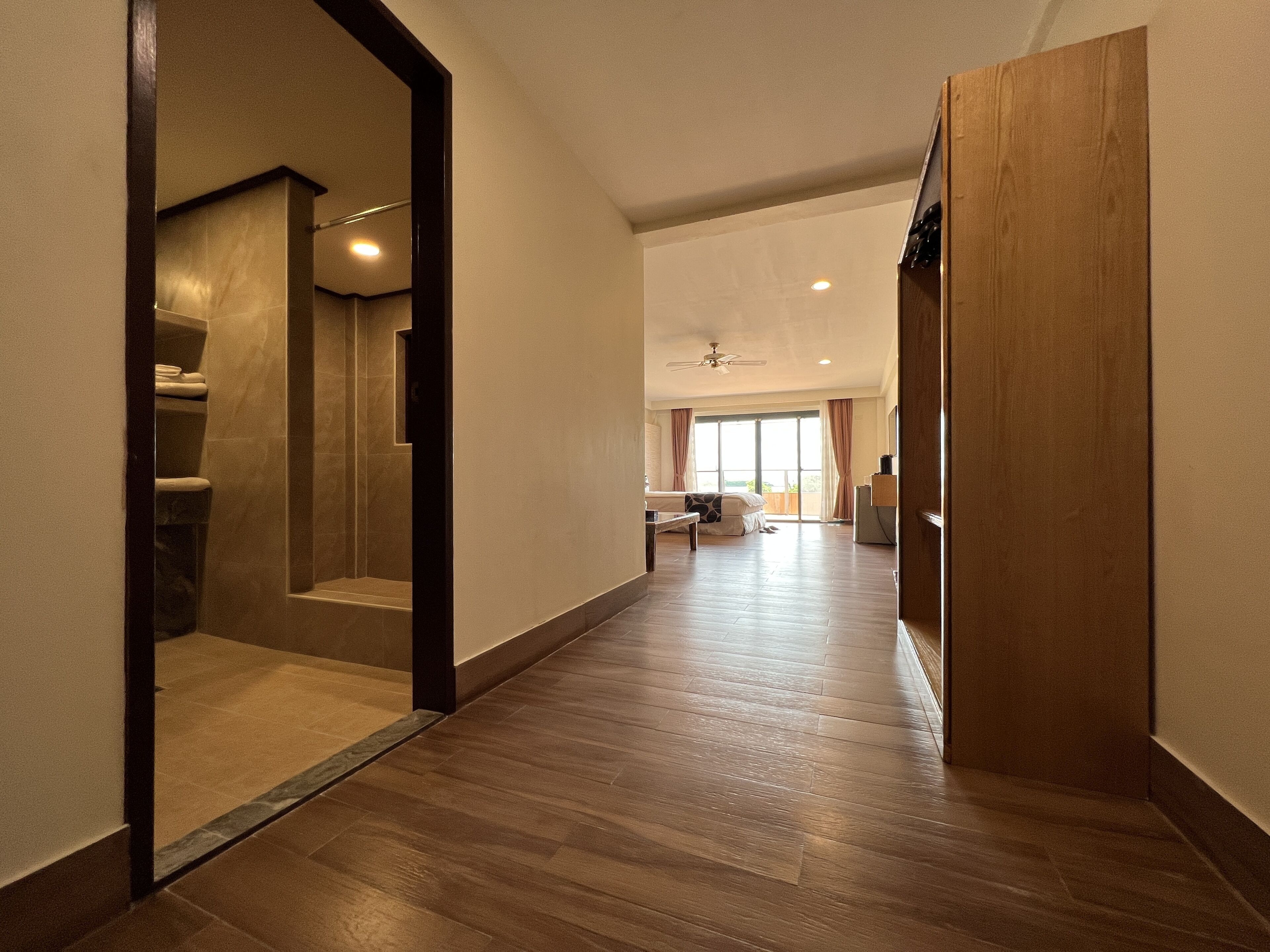 A hallway with a wooden floor leading to a bathroom with a shower and a toilet.