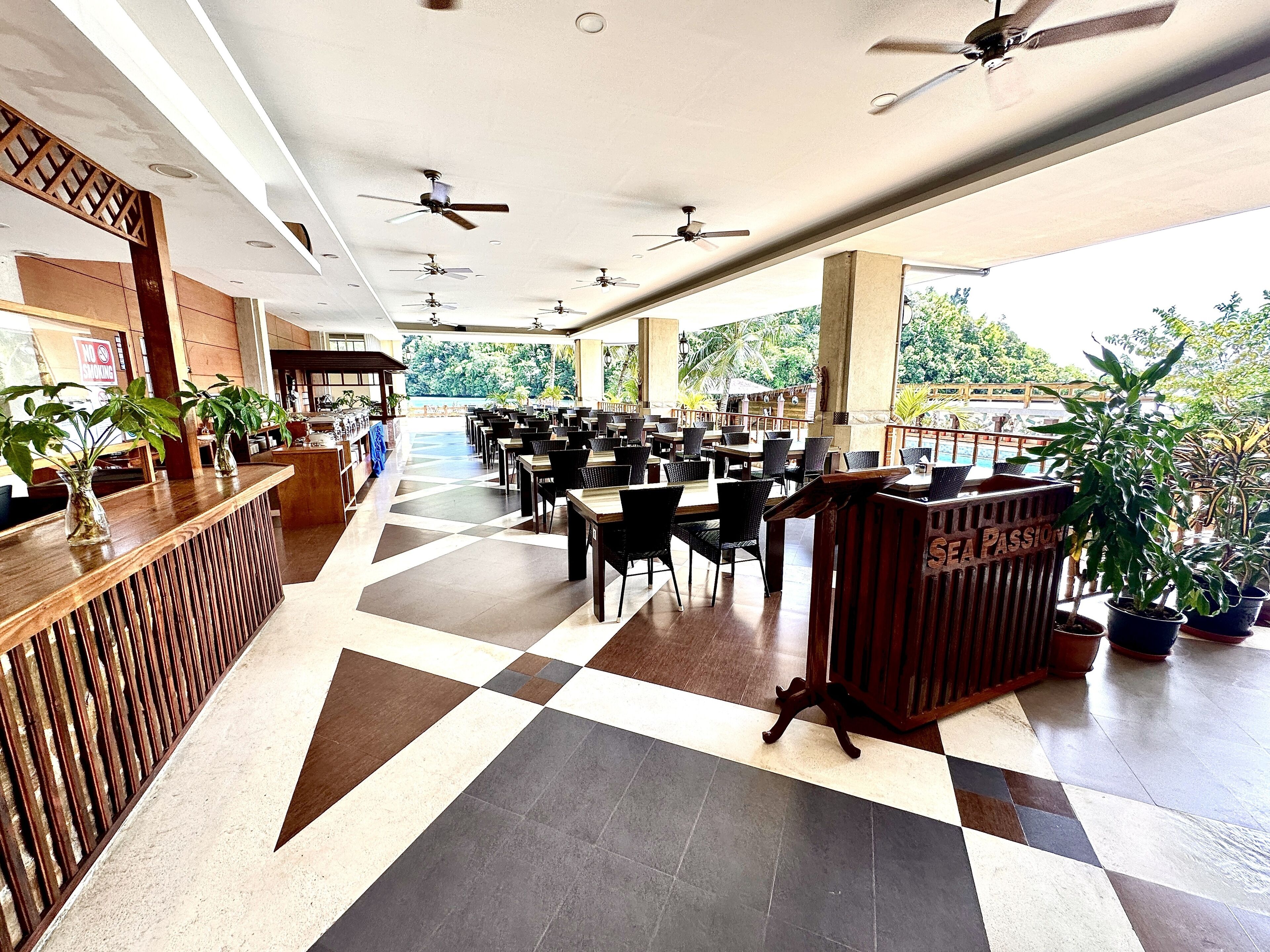 A spacious indoor area with multiple tables and chairs, ceiling fans, and potted plants.