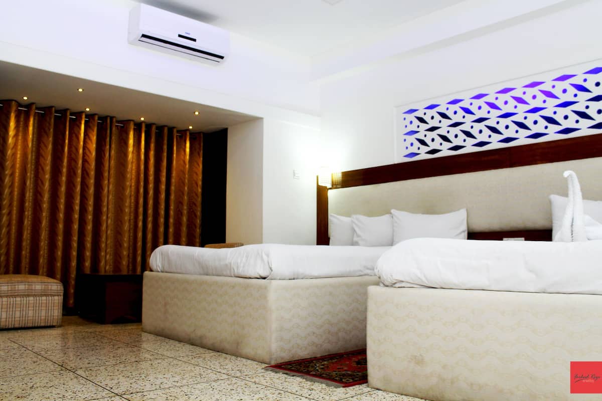 A hotel room with a bed, two bedside tables, a small sofa, a patterned rug, and a decorative wall panel.