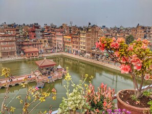 A riverside view of a historic city with traditional buildings, a small boat dock, and a gazebo. - Tajaa Pha The Heritage Home (Lalitpur)