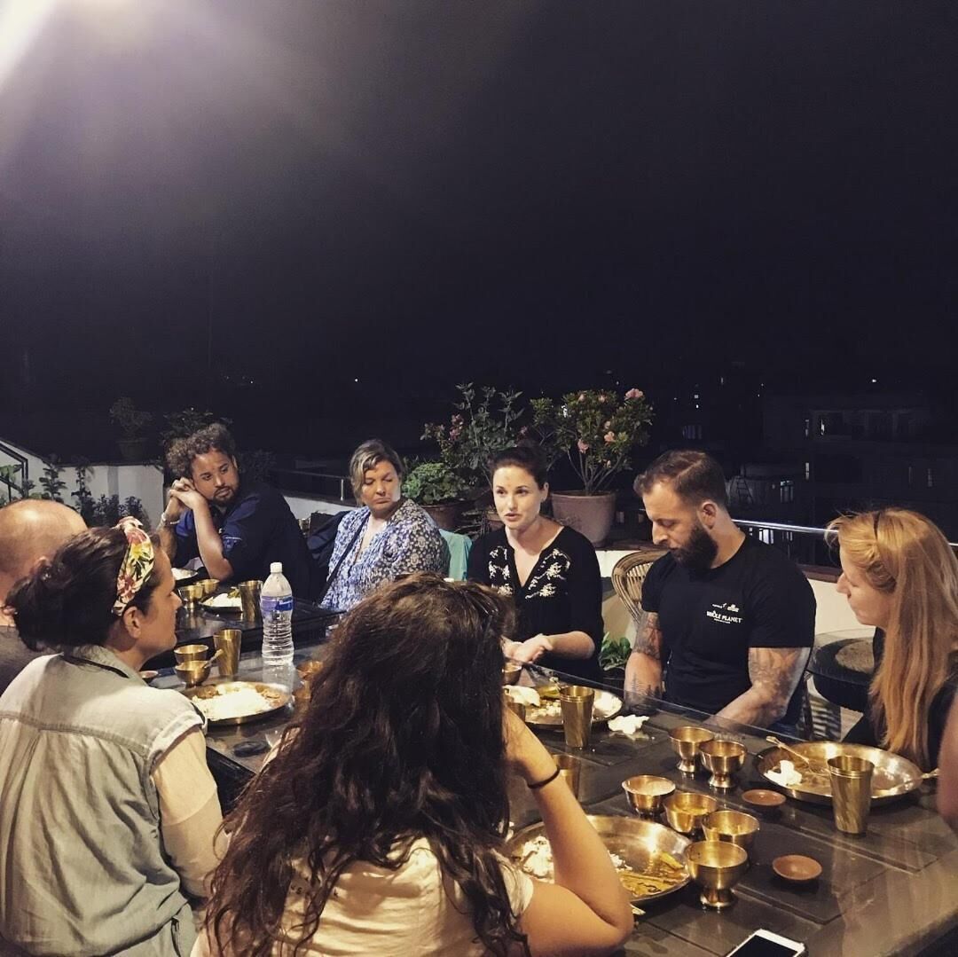 Un groupe de personnes dînant en plein air, la nuit, autour d’une table dressée avec différents plats et couverts.