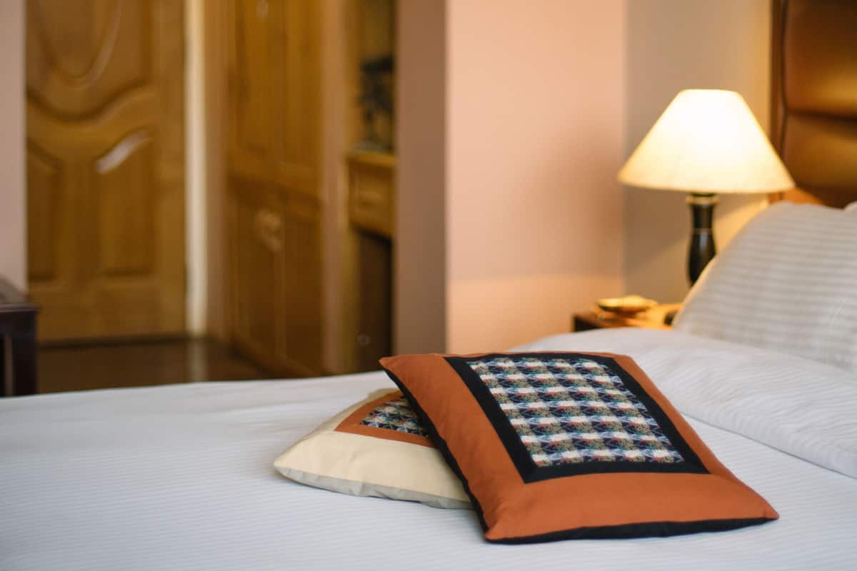 A neatly made bed with a pillow and a quilt, a bedside lamp, and a wooden door in the background.