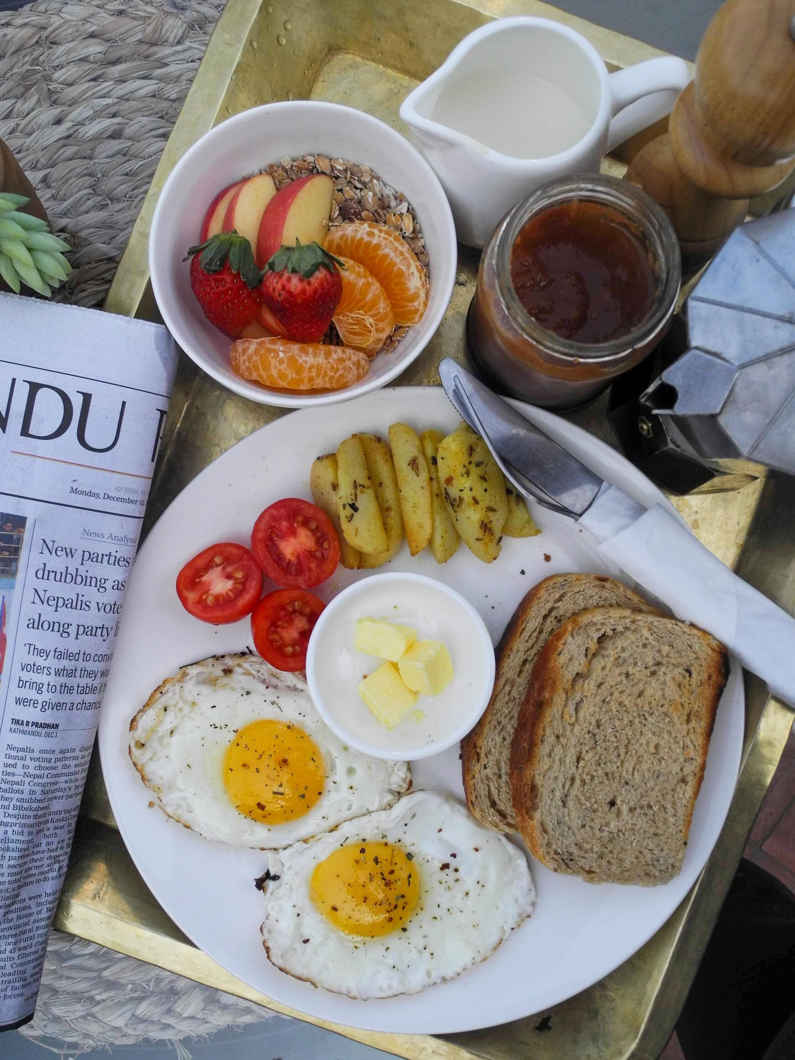 A breakfast plate with eggs, toast, tomatoes, potatoes, and a bowl of fruit.