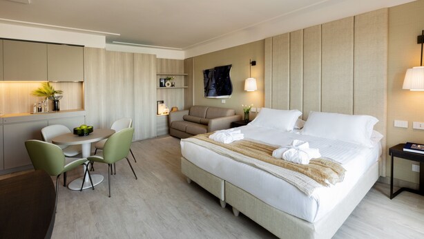 A modern hotel room with a large bed, a dining area with a round table and chairs, a sofa, and a small desk with a lamp. - Hotel Ceccarini 9 (Riccione)