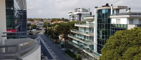 A modern urban street with multi-story buildings, a pedestrian walkway, and a car parked on the side.