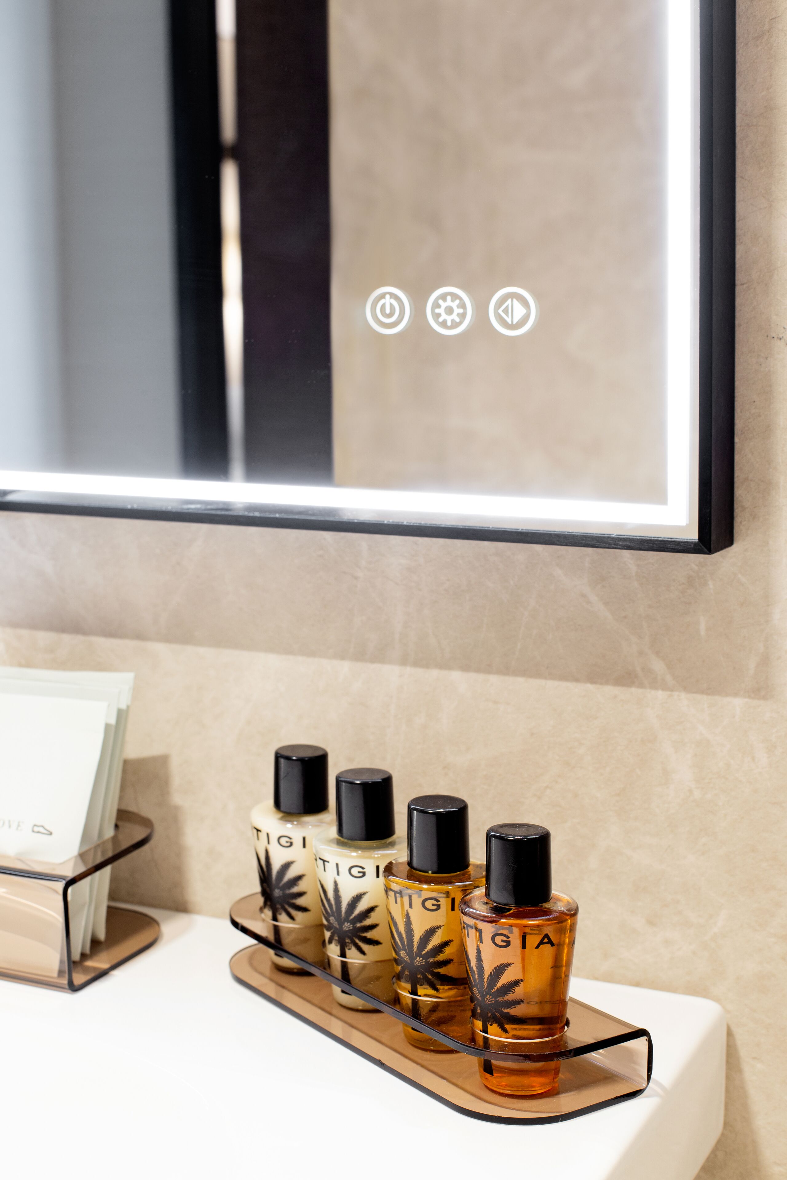 Un baño con un espejo, un estante con tres botellas de perfume Tigi y una caja blanca.