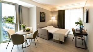 A hotel room with a bed, a desk, a chair, a small table, a lamp, and a view of the outside. - Hotel Ceccarini 9 (Riccione)