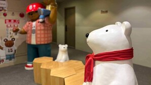A white bear figurine with a red scarf in a lobby area with wooden furniture and a person in a red cap. - Dazz Inn (Taichung)