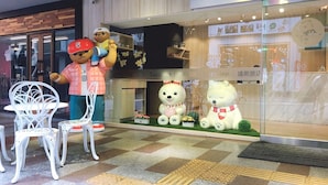 A storefront with a large teddy bear statue, a white chair, and a small garden display. - Dazz Inn (Taichung)
