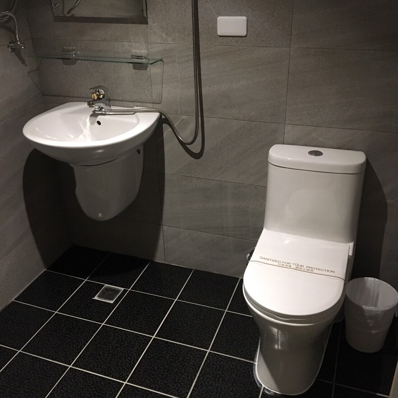 Une salle de bain avec un lavabo blanc, des toilettes et une poubelle.