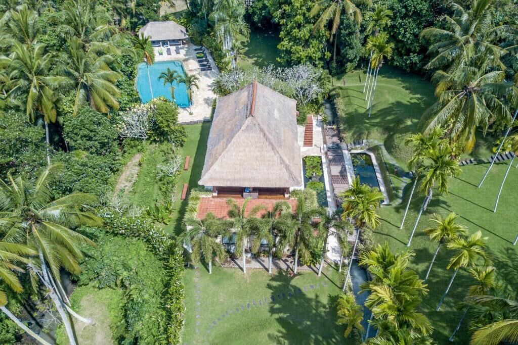 Vista aérea de un resort con piscina, edificio de techo de paja y palmeras.