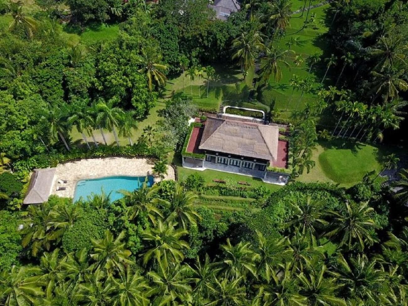 An aerial view of a resort with a swimming pool, lush greenery, and a large building with a red roof.