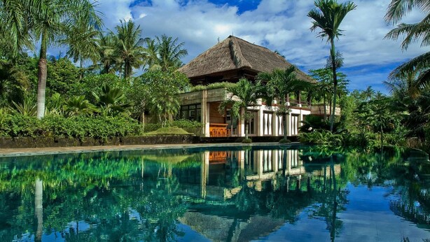 Um resort com piscina, palmeiras e um prédio com telhado de palha.