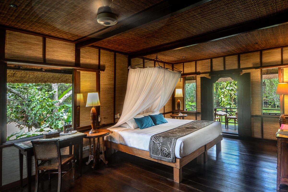 Une chambre à coucher avec un lit à baldaquin, des meubles en bois et une vue sur la verdure environnante.