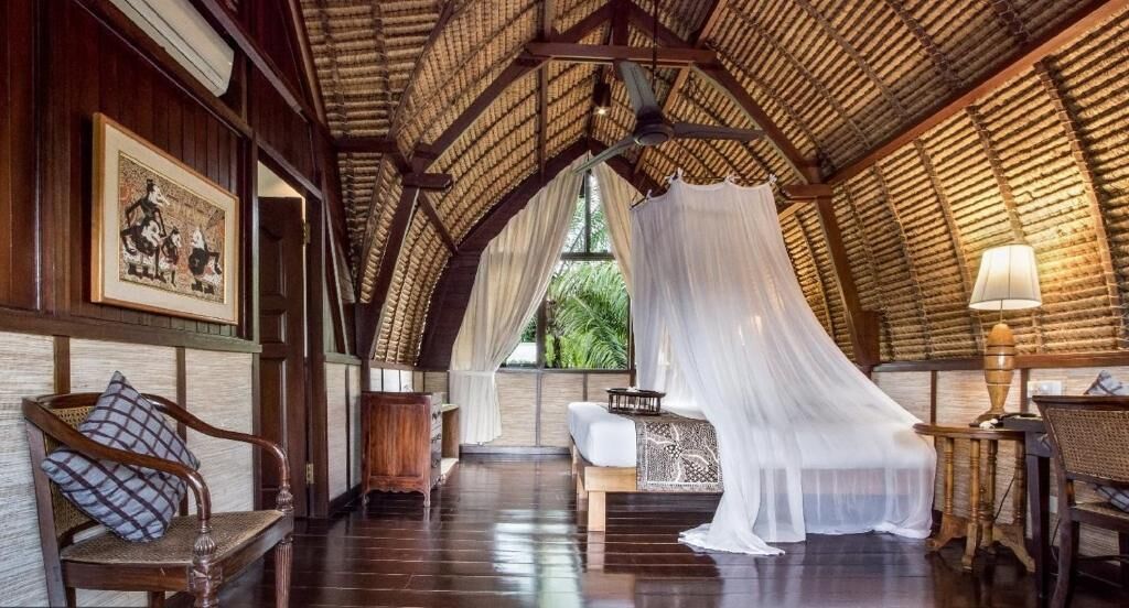 Una stanza con soffitto alto, travi in legno, un letto a baldacchino, una sedia, un tavolo e una lampada.