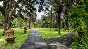 Um caminho pavimentado em um jardim exuberante, com palmeiras e lanternas decorativas.
