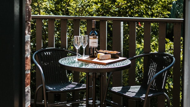 Un balcon avec une table ronde et deux chaises, une bouteille de vin et deux verres posés sur la table.