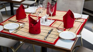 A dining table set with red napkins, white plates, and clear glasses, with a bamboo placemat and gold-toned cutlery. - Suriya Arana (Negombo)