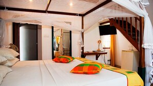 A bedroom with a bed, pillows, a desk, a chair, a television, and a staircase. - Suriya Arana (Negombo)