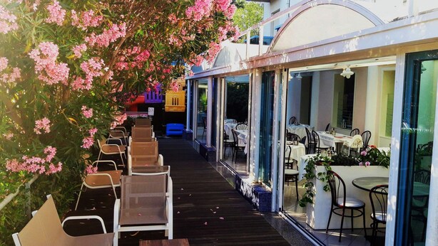 An outdoor dining area with tables and chairs, a wooden deck, and a glass-enclosed restaurant. - Hotel Felix (Rimini)