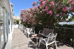 Un espacio al aire libre con mesas y sillas, una terraza de madera y un árbol grande con flores.