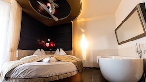 A modern bedroom with a large bed, a round bathtub, and a wall-mounted mirror. - Maiers Kuschelhotel deluxe - Adults only (Jennersdorf)