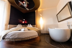 Een moderne slaapkamer met een groot bed, een rond ligbad en een spiegel aan de muur.