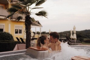 A couple in a hot tub with a palm tree and a yellow building in the background. - Maiers Kuschelhotel deluxe - Adults only (Jennersdorf)