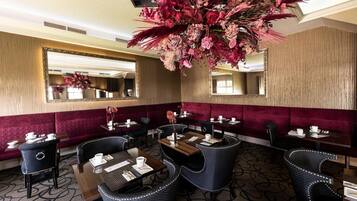 En hotellrestaurang med runda bord, svarta stoppade stolar och en stor blomsterdekoration i mitten.