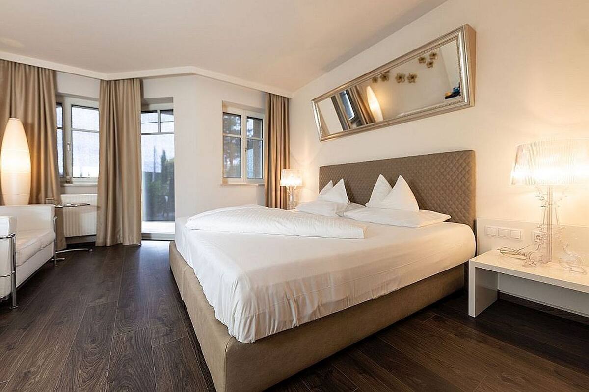 Quarto de hotel com uma cama grande, duas mesas de cabeceira com luminárias, uma cadeira e um espelho grande na parede.