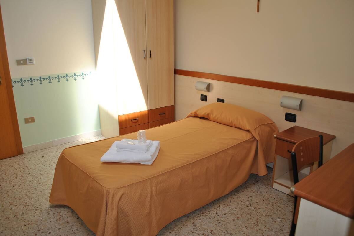 Una habitación de hotel con una cama, una mesita de noche, un armario de madera y una ventana con cortinas.