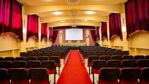 Un teatro con hileras de asientos, alfombra roja y un escenario con cortinas.