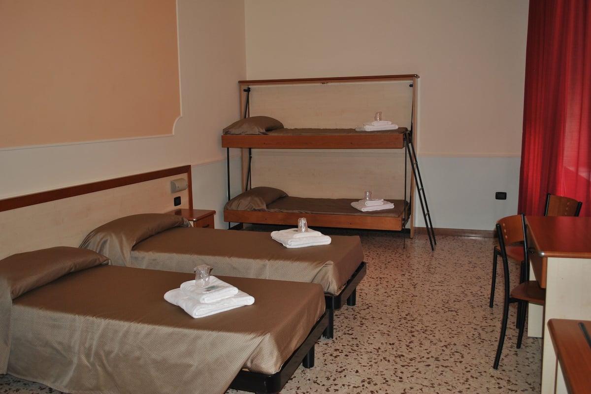 Una habitación de hotel con dos camas individuales, una litera y un escritorio con una silla.