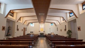 Interior de una iglesia con bancos de madera dispuestos en filas, un altar central y una cruz al frente.