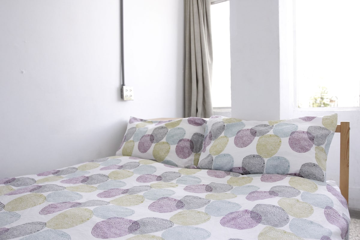 A bed with a polka dot bedspread, a wooden headboard, and a window with curtains.