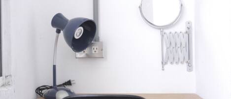 A desk with a black chair, a blue desk lamp, a round mirror, and a radiator.