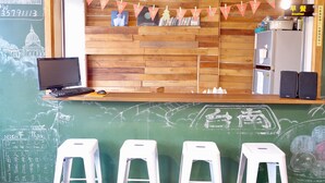 Un espace bar avec un comptoir en bois, des tabourets, un ordinateur portable et un mur noir où sont écrits des messages et dessinés des motifs.