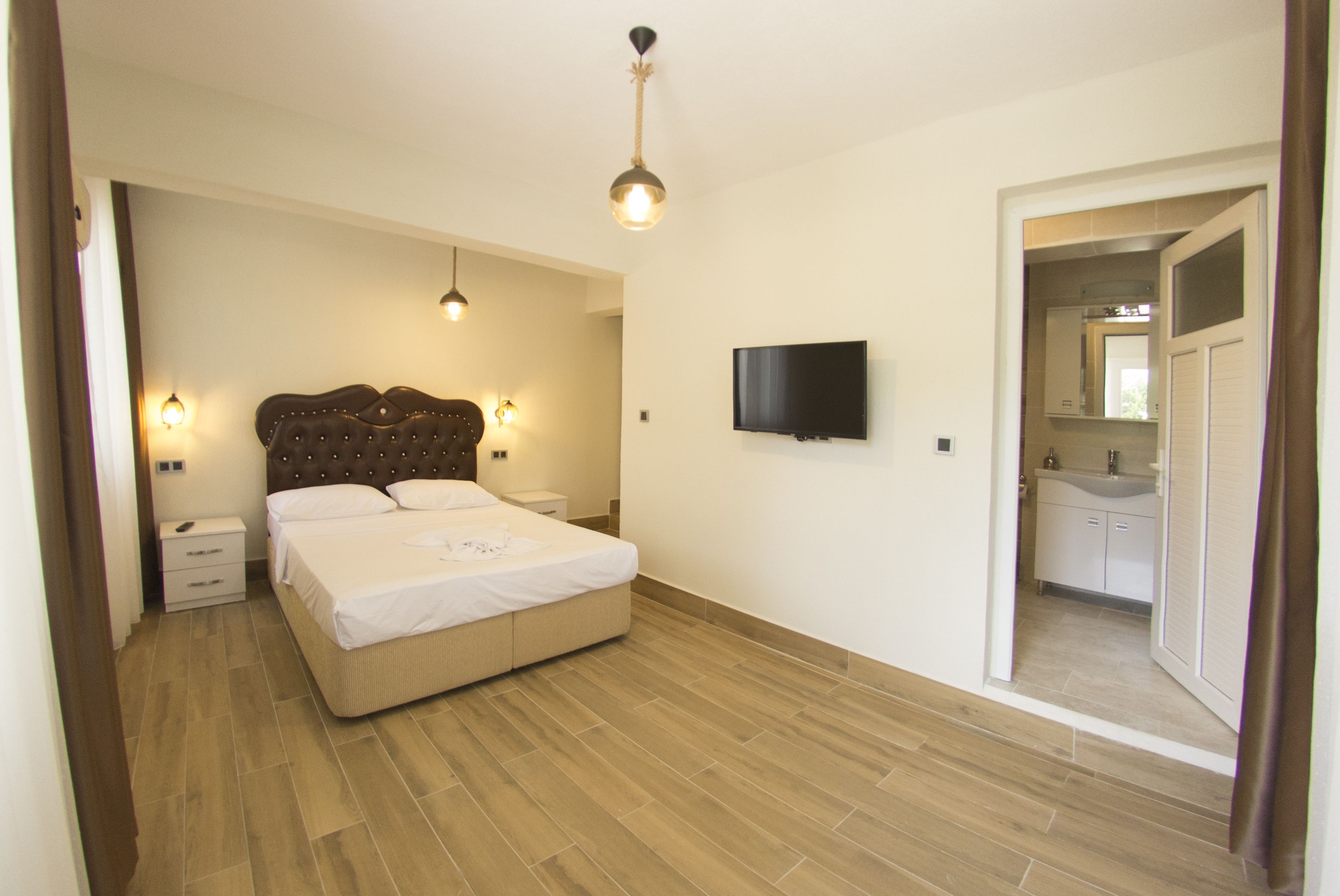 Un dormitorio con una cama grande, mesitas de noche, un televisor y un baño visible a través de una puerta abierta.