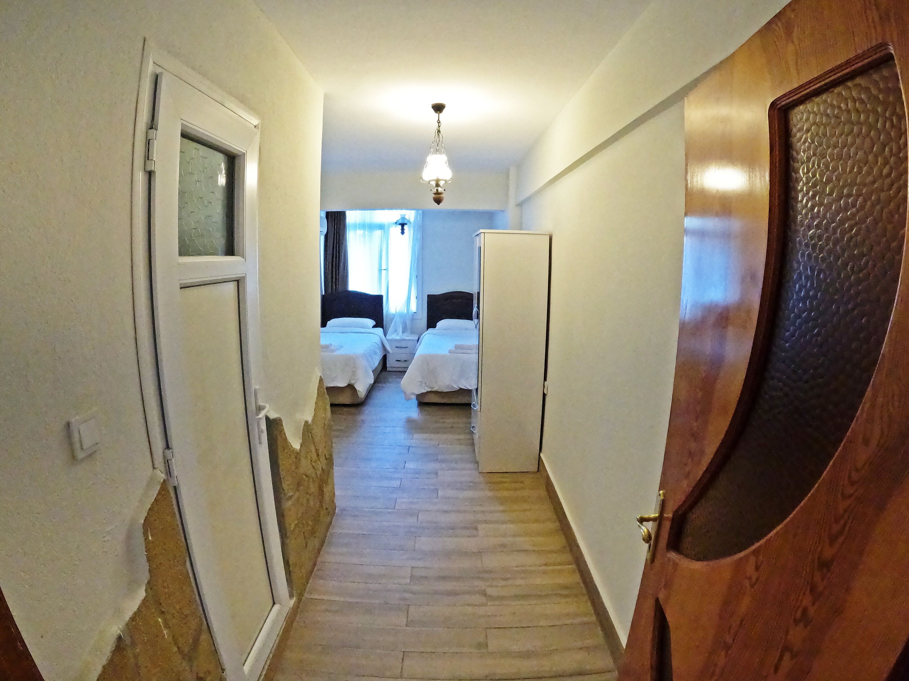 Un pasillo estrecho que conduce a un dormitorio con dos camas, una puerta de madera y una lámpara en el techo.