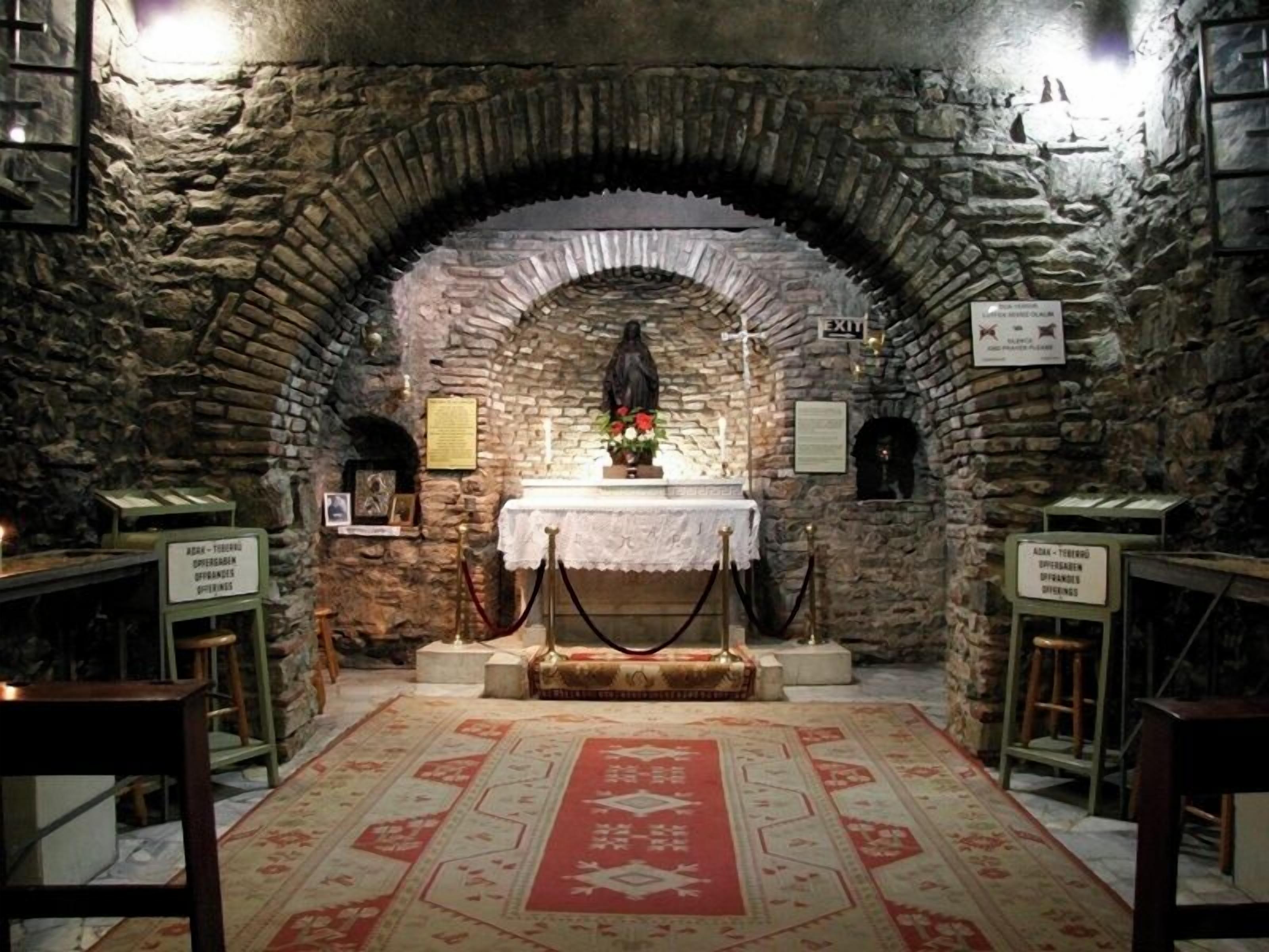 A stone-walled room with a central altar, a red patterned carpet, and informational signs.