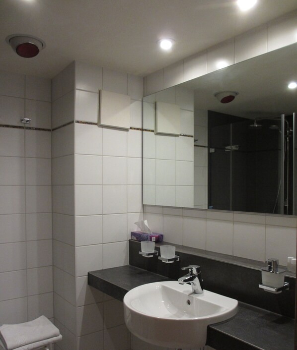 A modern bathroom with white tiles, a large mirror, a sink, and a shower.