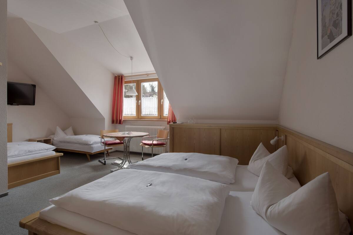 Ein Hotelzimmer mit zwei Betten, einem kleinen Tisch, einem Sessel, einem Fernseher und einem Fenster mit Vorhängen.