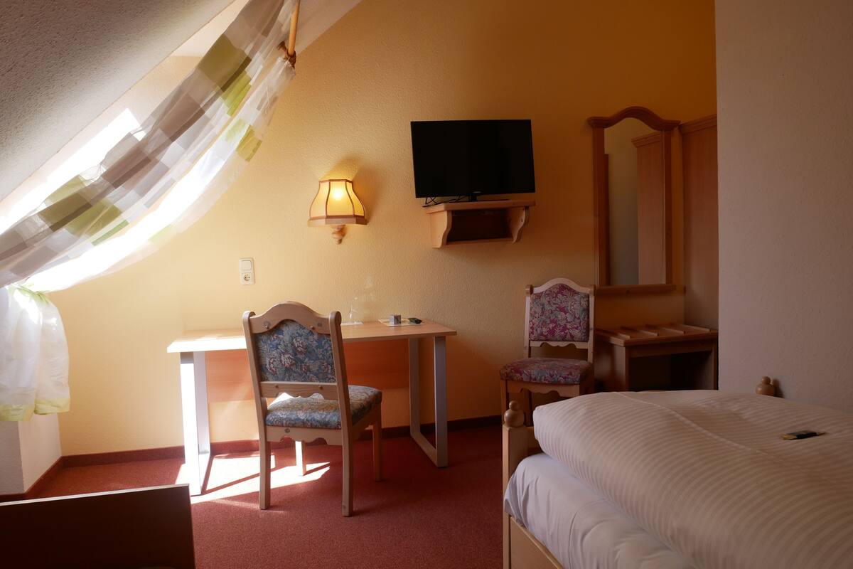 Ein Hotelzimmer mit Bett, Schreibtisch, Stuhl, Fernseher und Spiegel.