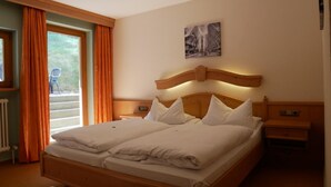 A double bed with a wooden headboard, two bedside tables, a radiator, and a window with orange curtains. - Hotel Gasthof Hereth (Wirsberg)