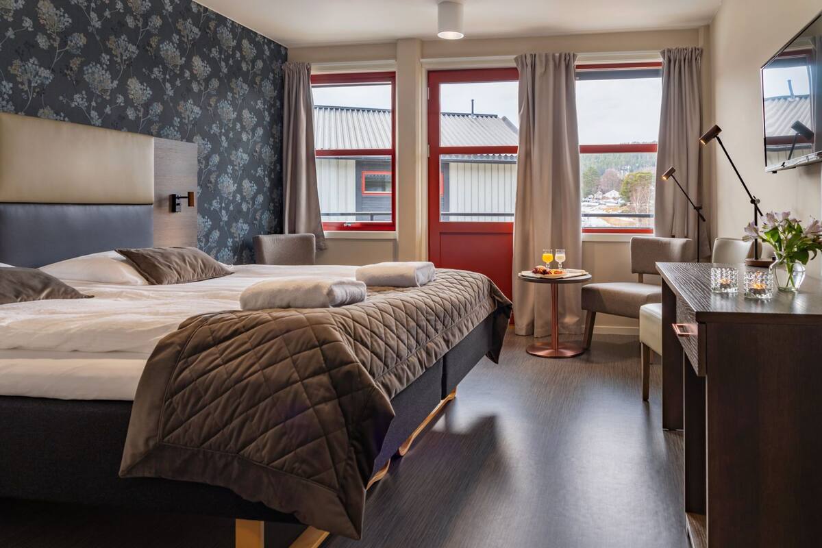 A hotel room with a bed, bedside tables, a desk, and a view of the outside.