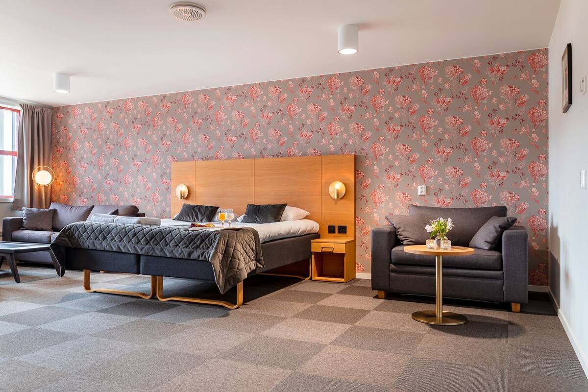 A modern hotel room with a large bed, a sofa, a round coffee table, and a small side table.