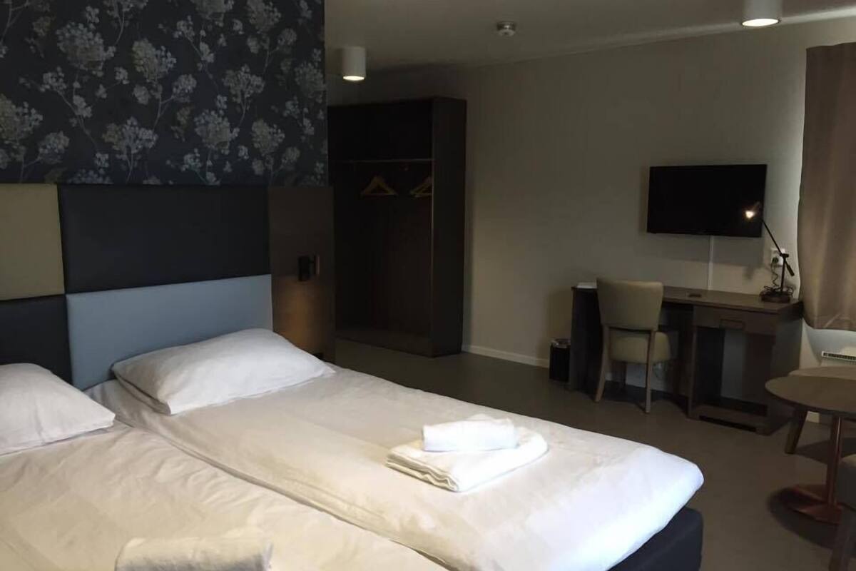 A hotel room with two beds, a desk, a chair, a TV, and a wardrobe.